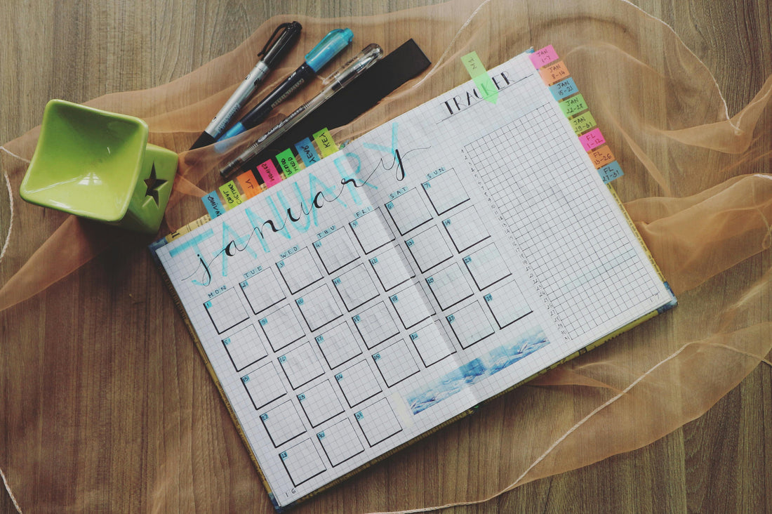 Monthly planner spread for January on grid paper with colorful sticky tabs, pens, and markers on a wooden desk.