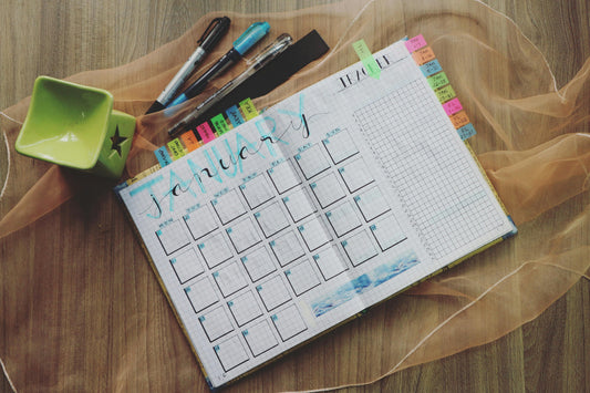 Monthly planner spread for January on grid paper with colorful sticky tabs, pens, and markers on a wooden desk.